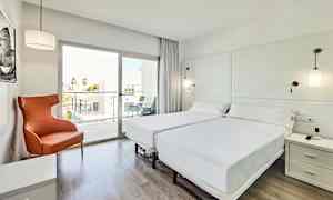 Valoisa ja moderni hotellihuone, jossa kaksi erillistä vuodetta, oranssi nojatuoli ja lasinen ikkuna, joka johtaa parvekkeelle. (Tekoälyn luoma teksti)