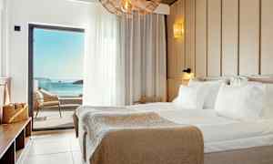 Hotellihuone, jossa suuri sänky ja merinäköala parvekkeen ovesta. (Tekoälyn luoma teksti)