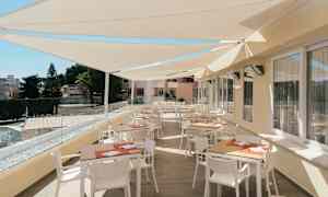 Terassi, jossa pöytiä ja tuoleja aurinkosuojakatoksen alla. (Tekoälyn luoma teksti)