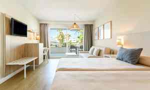 Hotellihuone, jossa on kaksi sänkyä, oleskelualue ja parveke näkymällä. (Tekoälyn luoma teksti)