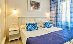 Kuva makuuhuoneesta, jossa kaksi erillistä sänkyä, sininen tyyny ja peitto sekä siniset verhot. (Tekoälyn luoma teksti)