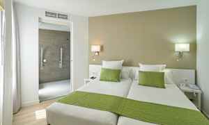 Hotellihuone jossa kaksi erillistä sänkyä, vihreät vuodevaatteet ja aukko kylpyhuoneeseen. (Tekoälyn luoma teksti)