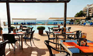 Ulkoravintola, jossa pöytiä ja tuoleja lähellä uima-allasta ja merta. (Tekoälyn luoma teksti)