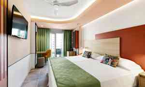 Moderni hotellihuone, jossa on kaksi vuodetta, vihreää sisustusta ja parveke näkymällä. (Tekoälyn luoma teksti)