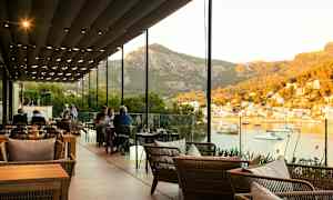 Ravintola ulkoistumapaikoilla katoksen alla, näkymä satamaan ja vuoristo taustalla. (Tekoälyn luoma teksti)