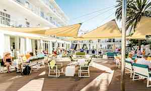 Ulkoterassi rakennuksen vieressä, jossa on pöytiä, tuoleja ja varjoa antavat kankaat. (Tekoälyn luoma teksti)