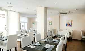 Valoisa ravintolatila, jossa on valkoiset tuolit ja tummat pöydät, katettu astioilla ja koristeilla. (Tekoälyn luoma teksti)