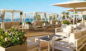 Lounge-alue, jossa istuinryhmiä ja aurinkotuoleja varjojen alla, sekä merinäköala. (Tekoälyn luoma teksti)