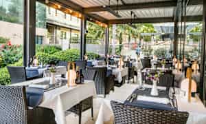 Ulkoterassi ravintola, jossa on katettuja pöytiä ja koristeltuja tuoleja. (Tekoälyn luoma teksti)