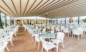 Ulkona oleva ravintola, jossa on paljon valkoisia pöytiä ja tuoleja katon alla. (Tekoälyn luoma teksti)