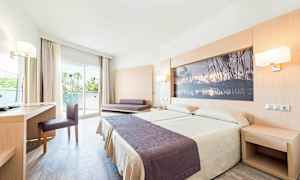 Hotellihuone, jossa on parivuode, kirjoituspöytä, tuoli ja sohva. Huoneessa on lasiovi, joka johtaa parvekkeelle. (Tekoälyn luoma teksti)