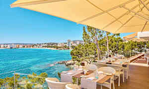 Ulkoterassi, josta on näkymä kirkkaansiniseen lahtimereen ja taustalla oleviin rakennuksiin. (Tekoälyn luoma teksti)