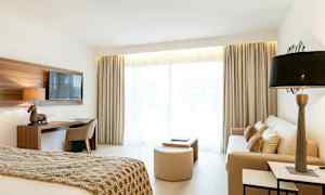 Kuva valoisasta hotellihuoneesta, jossa on sänky, sohva ja kirjoituspöytä. (Tekoälyn luoma teksti)