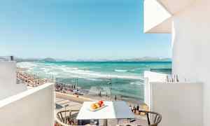 Näkymä parvekkeelta rannalle, turkoosiin veteen, hiekkaan ja ihmisiin, jotka uivat. (Tekoälyn luoma teksti)