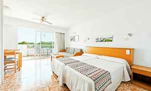 Hotellihuone, jossa on vaalea sisustus, kaksi yhden hengen vuodetta, sohva, pöytä ja tuoleja sekä parveke näköalalla. (Tekoälyn luoma teksti)