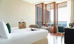 Hotellihuone, jossa on sänky, kirjoituspöytä tuoleineen ja parveke merinäköalalla. (Tekoälyn luoma teksti)