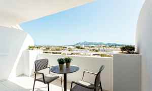 Parveke, jossa pöytä ja tuolit, näkymä ympäröiviin rakennuksiin ja vuorille. (Tekoälyn luoma teksti)