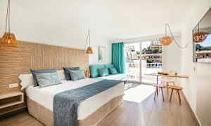 Hotellihuone, jossa on parivuode, sohva tyynyineen, pieni ruokailutila ja parveke. (Tekoälyn luoma teksti)