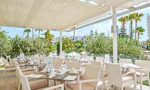 Ravintola, jossa valkoiset huonekalut ja katto, ympäröitynä vehreydellä. (Tekoälyn luoma teksti)