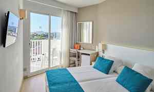 Valoisa hotellihuone, jossa kaksi sänkyä, siniset tyynyt ja päiväpeitteet sekä parveke näkymällä. (Tekoälyn luoma teksti)