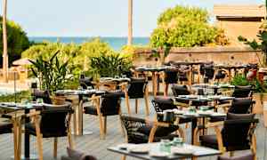 Ulkoterassi, jossa pöytiä, tuoleja ja vihreitä kasveja. (Tekoälyn luoma teksti)