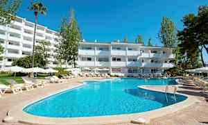 Ulkoallas, jonka ympärillä on aurinkotuoleja ja aurinkovarjoja valkoisen rakennuksen edustalla, puiden ympäröimänä. (Tekoälyn luoma teksti)