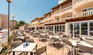 Terassiravintola pöytineen ja tuoleineen, jota ympäröi rakennus, jossa on parvekkeita. (Tekoälyn luoma teksti)