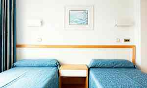 Kaksi erillistä vuodetta sinisillä päiväpeitteillä ja taustalla puinen paneeli. (Tekoälyn luoma teksti)