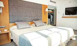 Kuva, jossa on moderni hotellihuone, jossa on parivuode, vaatekaappi ja seinälle asennettu televisio. (Tekoälyn luoma teksti)