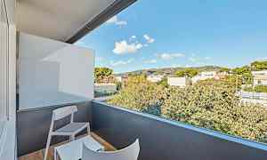 Parveke, jossa on kaksi tuolia ja pöytä, näköala ympäröiviin puihin ja rakennuksiin sinisen taivaan alla. (Tekoälyn luoma teksti)