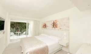 Vaalea hotellihuone, jossa on parivuode, seinäkoriste simpukoiden teemalla ja parveke lasiovien ulkopuolella. (Tekoälyn luoma teksti)