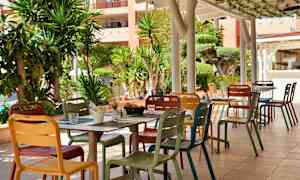 Ulkoilma-alue, jossa on värikkäitä tuoleja ja pöytiä, ympärillä vehreitä kasveja. (Tekoälyn luoma teksti)