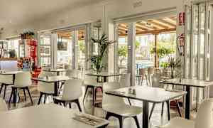 Ravintola, jossa on valkoiset tuolit ja pöydät, avoinna terassille ja ympäröivään vehreyteen. (Tekoälyn luoma teksti)