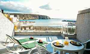 Terassi, jossa kaksi lepotuolia ja pöytä, jossa appelsiinimehua ja leivonnaisia, merenäköala taustalla. (Tekoälyn luoma teksti)