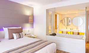 Hotellihuone, jossa on sänky ja sisäänrakennettu poreallas, joka avautuu kohti kylpyhuonetta. (Tekoälyn luoma teksti)