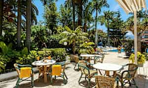 Ulkoilmaravintola pöytiä ja tuoleja lähellä uima-allasta ja vehreää kasvillisuutta. (Tekoälyn luoma teksti)