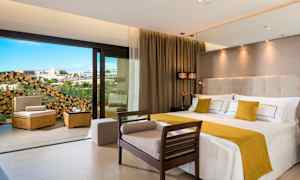 Nykyaikainen hotellihuone, jossa on suuri sänky ja istuimia sekä avautuminen parvekkeelle näkymineen. (Tekoälyn luoma teksti)