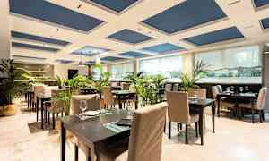 Tyylikäs ravintola-alue, jossa on pöytiä ja tuoleja, koristeltu vihreillä kasveilla. (Tekoälyn luoma teksti)