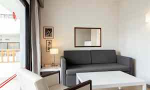 Olohuone, jossa on harmaa sohva ja valkoinen pöytä, nojatuoli ja parvekkeelle johtava lasiovi. (Tekoälyn luoma teksti)