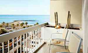 Parveke, jossa kaksi tuolia ja kukkalaatikko, jossa kaktuksia. Näkymä osoittaa rannan palmujen ja lahden kanssa. (Tekoälyn luoma teksti)