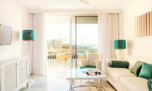 Valoisa olohuone, jossa sohva, pöytä ja tuolit sekä lasiovet, jotka johtavat parvekkeelle merinäköalalla. (Tekoälyn luoma teksti)