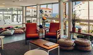 Valoisa huone, jossa on suuret ikkunat, kaksi oranssia nojatuolia ja koripallikkia kahvipöydän edessä. (Tekoälyn luoma teksti)