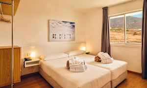 Vaalea hotellihuone, jossa on parivuode, ikkuna näkymällä maisemaan ja seinämaalaus sängyn yläpuolella. (Tekoälyn luoma teksti)