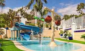 Vesileikkipaikka, jossa on sininen liukumäki ja vesivirtoja sekä koristeellisia palmuja. (Tekoälyn luoma teksti)