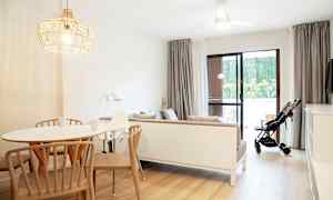 Valoisa ja modernisti sisustettu olohuone, jossa ruokapöytä, sohva ja lastenvaunut lasioven vieressä. (Tekoälyn luoma teksti)