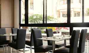 Ravintola, jossa on pöytiä ja tuoleja, ja näkymä sisäpihalle suuren ikkunan kautta. (Tekoälyn luoma teksti)