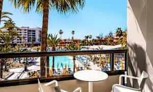 Näkymä parvekkeelta hotellialueelle, jossa on uima-allas ja aurinkotuoleja, ympäröitynä palmupuiden kanssa. (Tekoälyn luoma teksti)