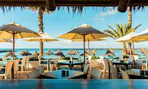 Ulkoilmaravintola rannalla, jossa on aurinkovarjoja ja merinäköala. (Tekoälyn luoma teksti)