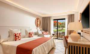 Valoisa ja tyylikäs hotellihuone, jossa on suuri sänky, koristetyynyt ja yksityinen ulkoseisonta-alue näkymällä puutarhaan. (Tekoälyn luoma teksti)