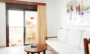 Huoneen sisustus, jossa on sohva, pöytä ja seinällä purjeveneistä tehty maalaus. Lasiovet johtavat parvekkeelle. (Tekoälyn luoma teksti)